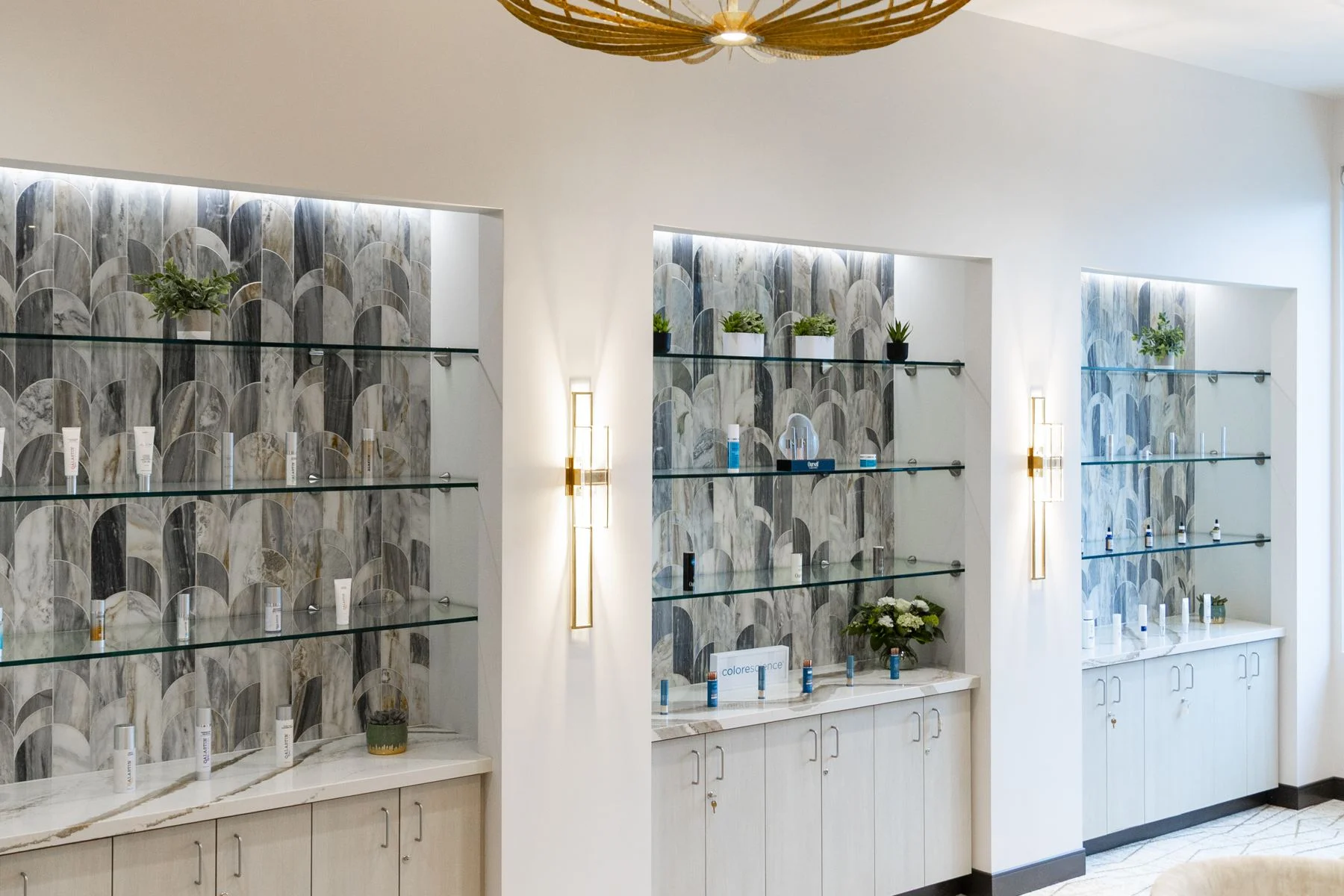 Backlit glass shelves of skin care products against mosaic tile in the Visalia skin care lounge